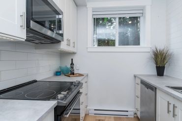 Modern kitchen with white cabinets, stainless steel appliances, and a window overlooking greenery.