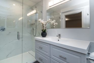 Modern bathroom with glass shower, white vanity, and orchid plant.