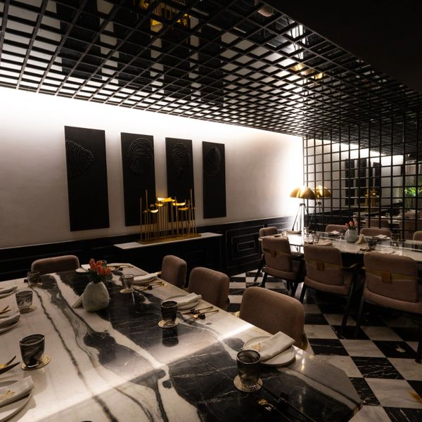 Elegant dining room with marble tables, modern chairs, and artistic decor under a lattice ceiling.