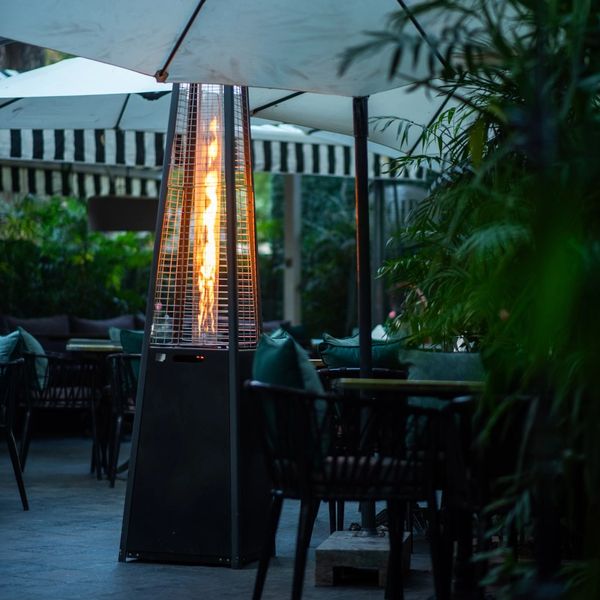 Outdoor patio heater with flame under umbrellas in a cozy seating area.