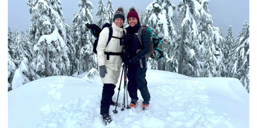 Two smiling women with snow-covered trees