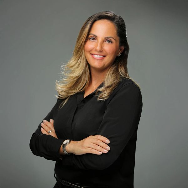 Confident woman with crossed arms smiles warmly in a professional portrait.
