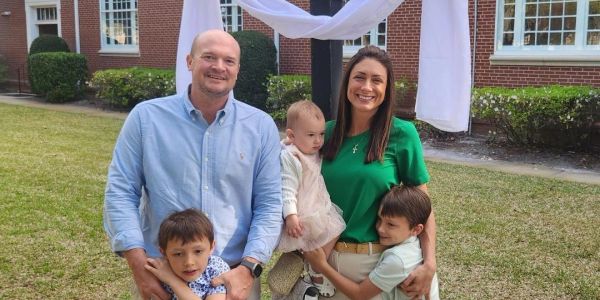 A happy family of five posing outdoors in front of a building with white decoration.