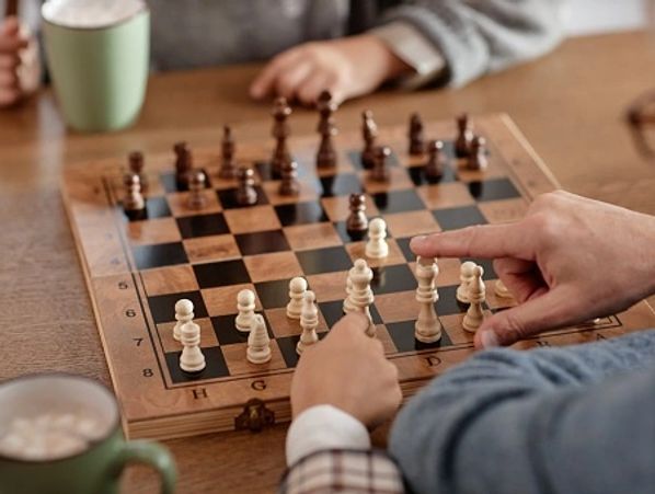 A person's hands are shown playing chess on a wooden board with another person.