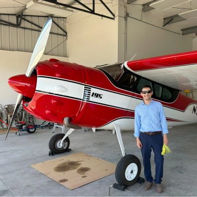 Man standing next to a red and white small aircraft inside a hangar.