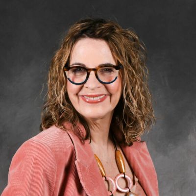 Smiling woman with curly hair and glasses in a pink jacket.