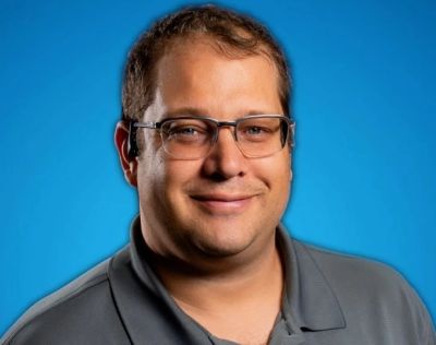 Smiling man wearing glasses and a gray polo shirt.