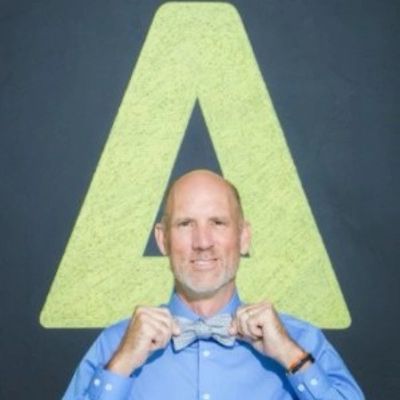 Man adjusting a bow tie in front of a large letter A.