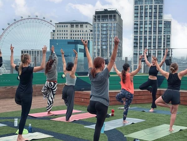 Group yoga session on rooftop with cityscape and Ferris wheel in background.