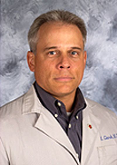 A middle-aged man in a lab coat with a serious expression.