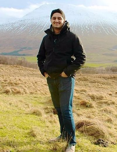 Man standing in a grassy field with snowy mountains in the background.