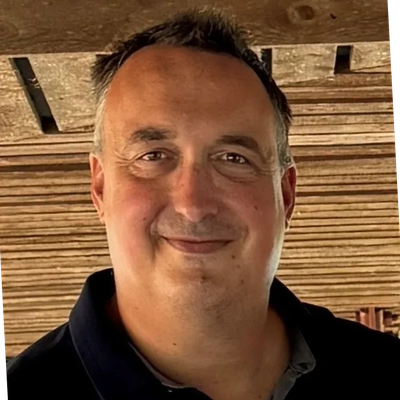 Smiling man in a casual setting with wooden background.