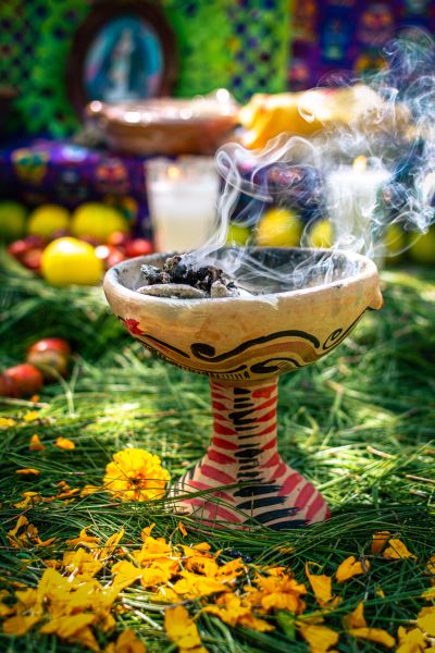 Decorative incense burner with smoke, surrounded by marigold petals and greenery.