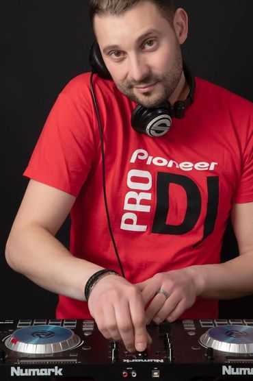 DJ in a red Pioneer Pro DJ shirt mixing music on Numark equipment.