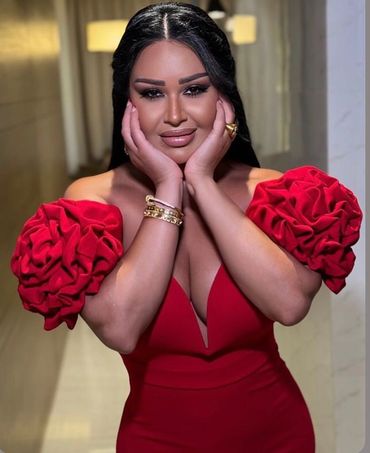 Woman in elegant red dress with floral puff sleeves, posing with hands on face.