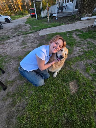 A woman happily hugs a golden retriever outside a house at sunset.