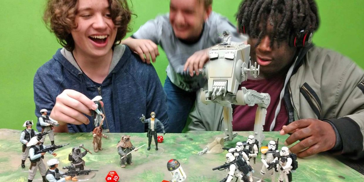 Three friends enjoy playing with Star Wars action figures on a tabletop battlefield.