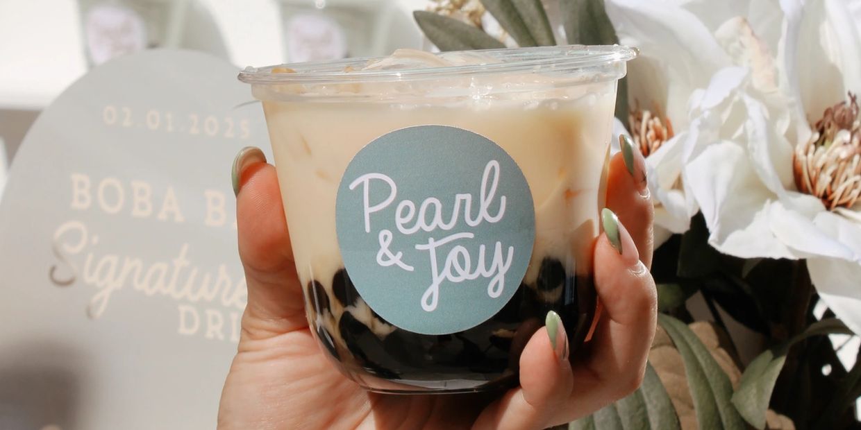 Hand holding a cup of iced bubble tea from Pearl & Joy with tapioca pearls.