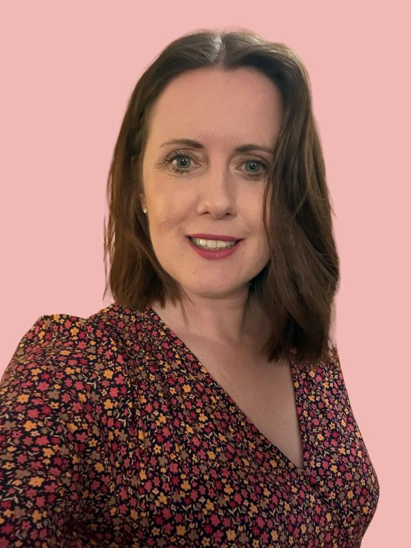 Lisa smiling with floral dress against a pink background.