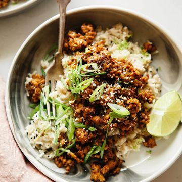 A bowl of crisp tempeh with rice, sliced shallots and a lime wedge