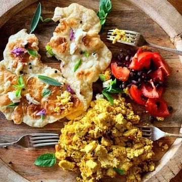scrambled tofu with chopped tomatoes and flatbread on a round board