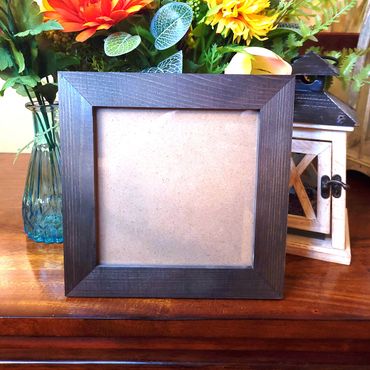 Empty wooden photo frame on a table with flowers and lantern.