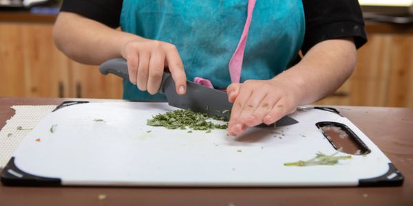 little cook chopping herbs with a large chefs knife
