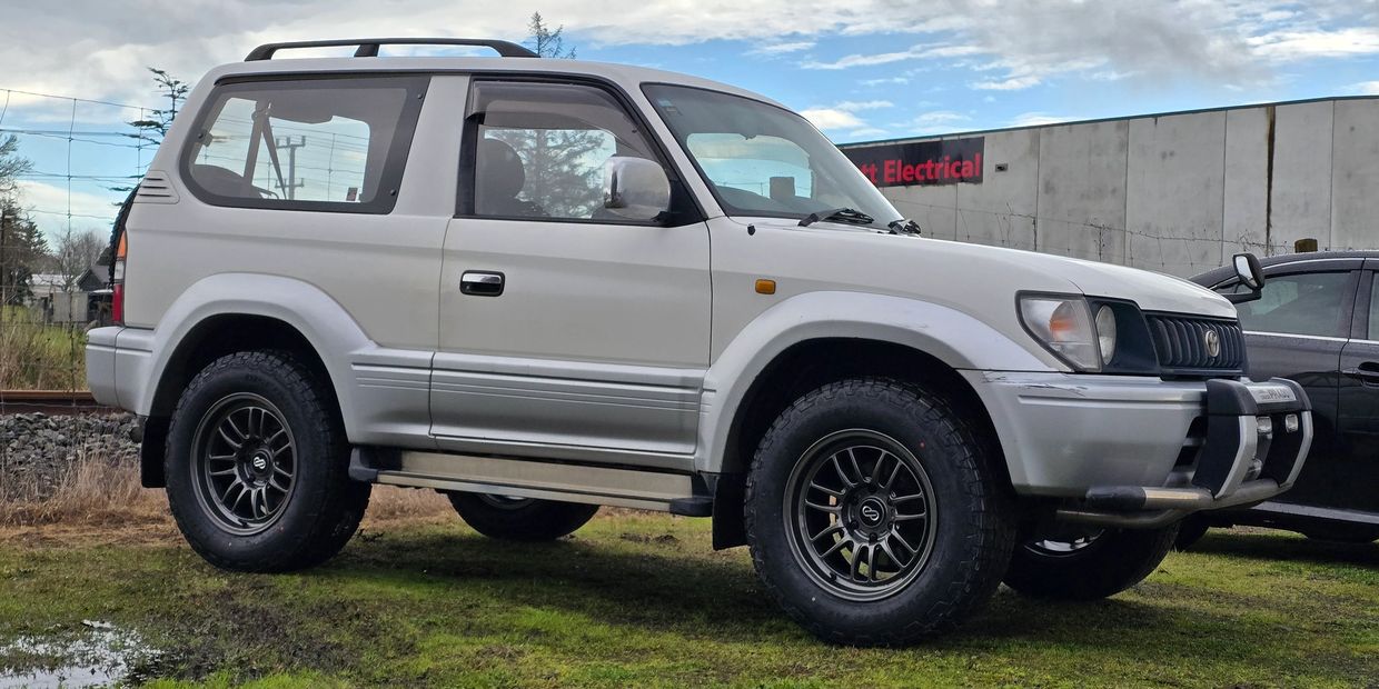 White off-road SUV parked on grass near a railway track.