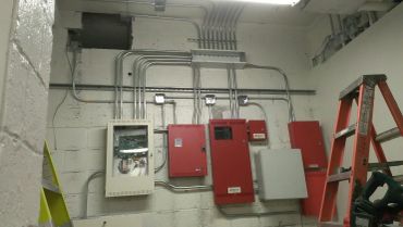 Fire Alarm panels and conduit pipes organized on a wall in a utility room.