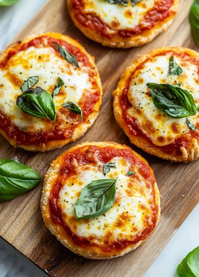 Vier mini pizza's met mozzarella en basilicum op een houten plank.