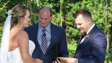 Bride and groom exchanging vows outdoors with officiant.
