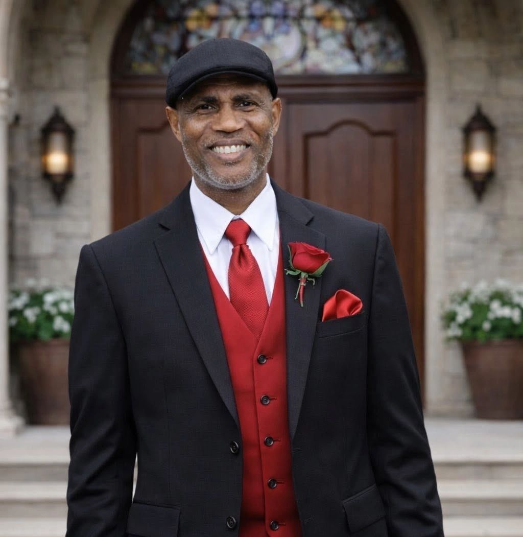 Man in black suit with red tie and boutonniere smiles.