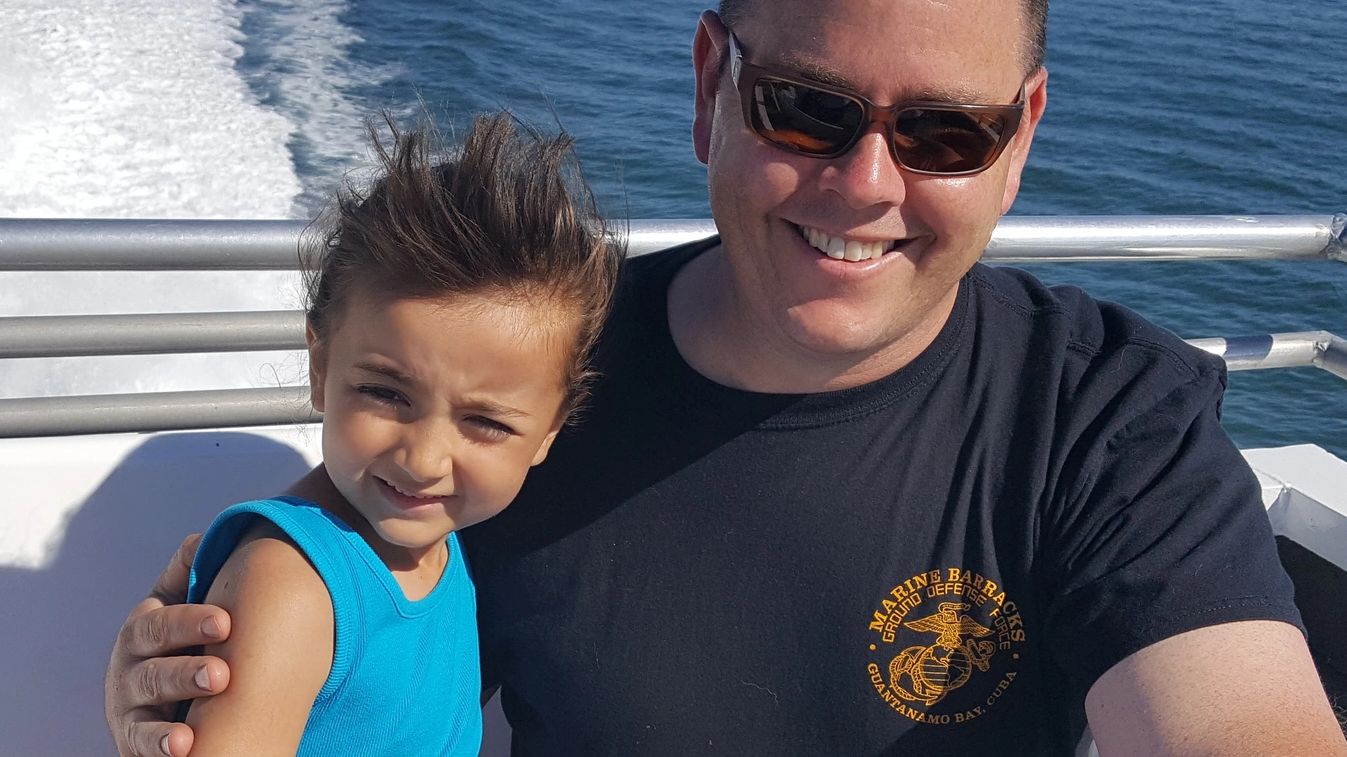 Smiling man and child on a boat with ocean background.