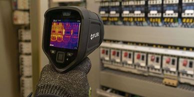 Hand holding a FLIR thermal camera scanning electrical panels.