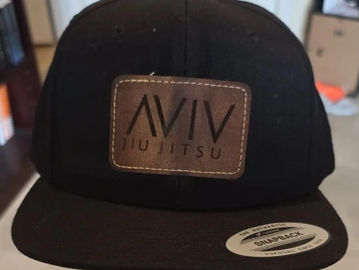 A flat bill hat with a laser etched leather patch heat pressed on to it