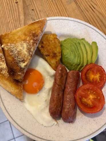 Breakfast plate with eggs, sausage, toast, hash brown, avocado, and tomato.