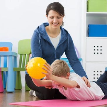 Occupational Therapist treating child holding yellow ball.  Child is lying on belly working reflexes