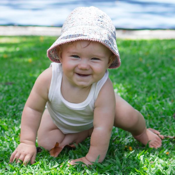 Smiling baby with hat crawling in grass