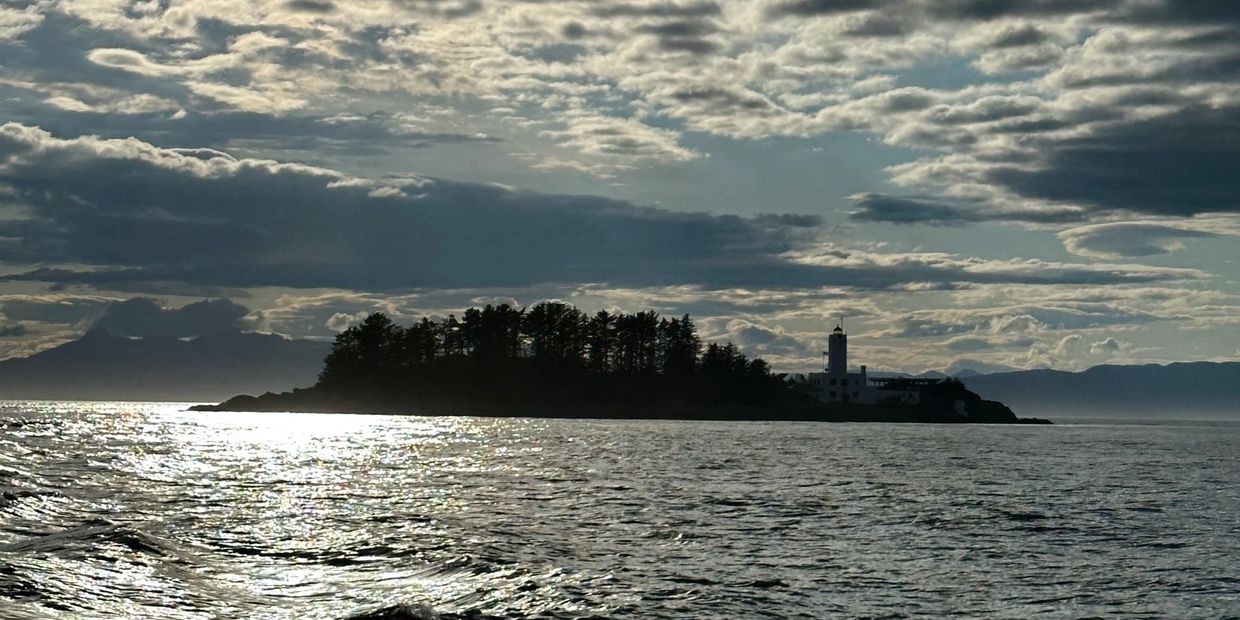 Silhouetted island and lighthouse with cloudy sky at sunset.