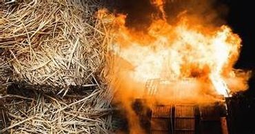 A barn engulfed in bright flames with dry hay nearby.
