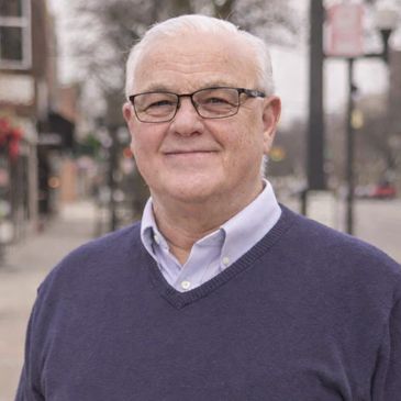 Smiling elderly man in glasses and sweater outdoors.