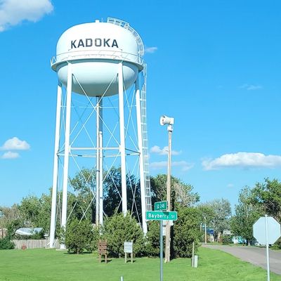 Tall white water tower labeled Kadoka in a small town setting.