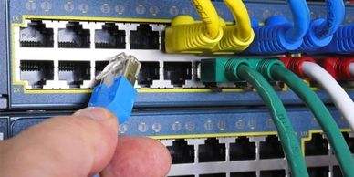 Hand plugging blue Ethernet cable into network switch ports.