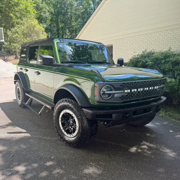 Green Bronco with bushes in background