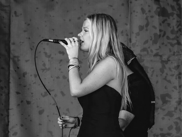 A woman passionately singing into a microphone on stage in black and white.