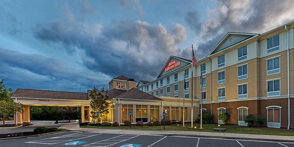 Exterior view of a Hampton Inn hotel at dusk with a dramatic cloudy sky.