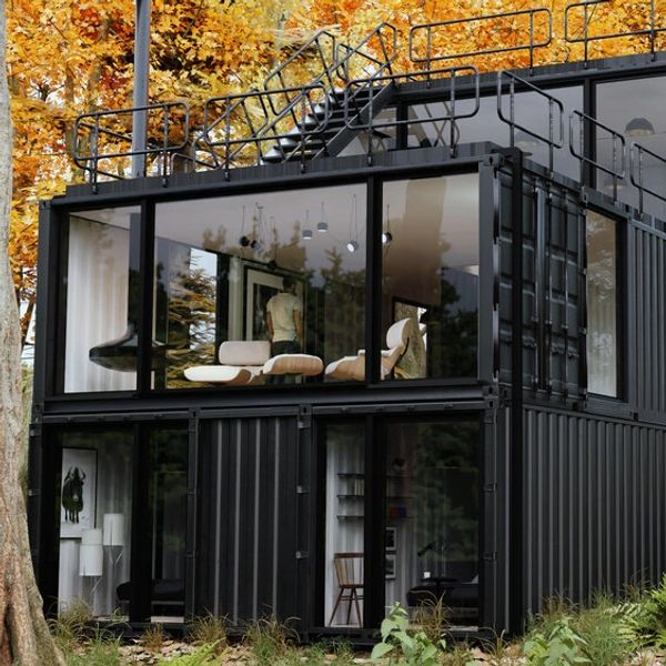 Modern black container home with large glass windows surrounded by autumn trees.