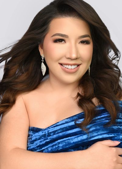 Smiling woman with long wavy hair wearing a blue velvet off-shoulder dress and sparkly earrings.