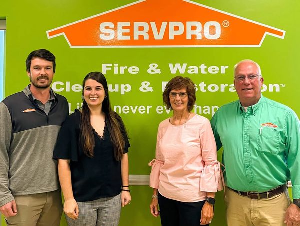 Four SERVPRO employees stand smiling in front of a green company wall.