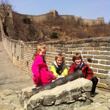 Three children sitting by a cannon on the Great Wall of China.